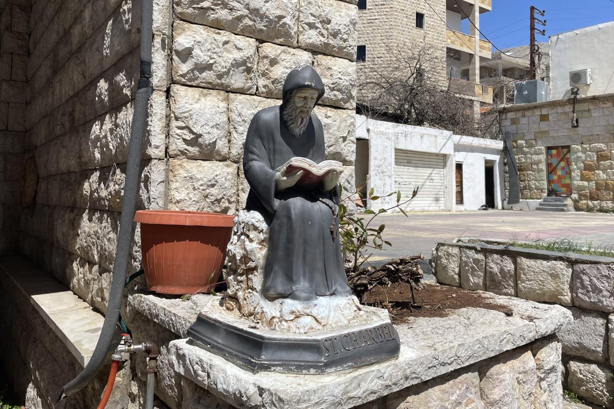 Statue of St. Charbel, a monk, seated and reading a book in his lap.