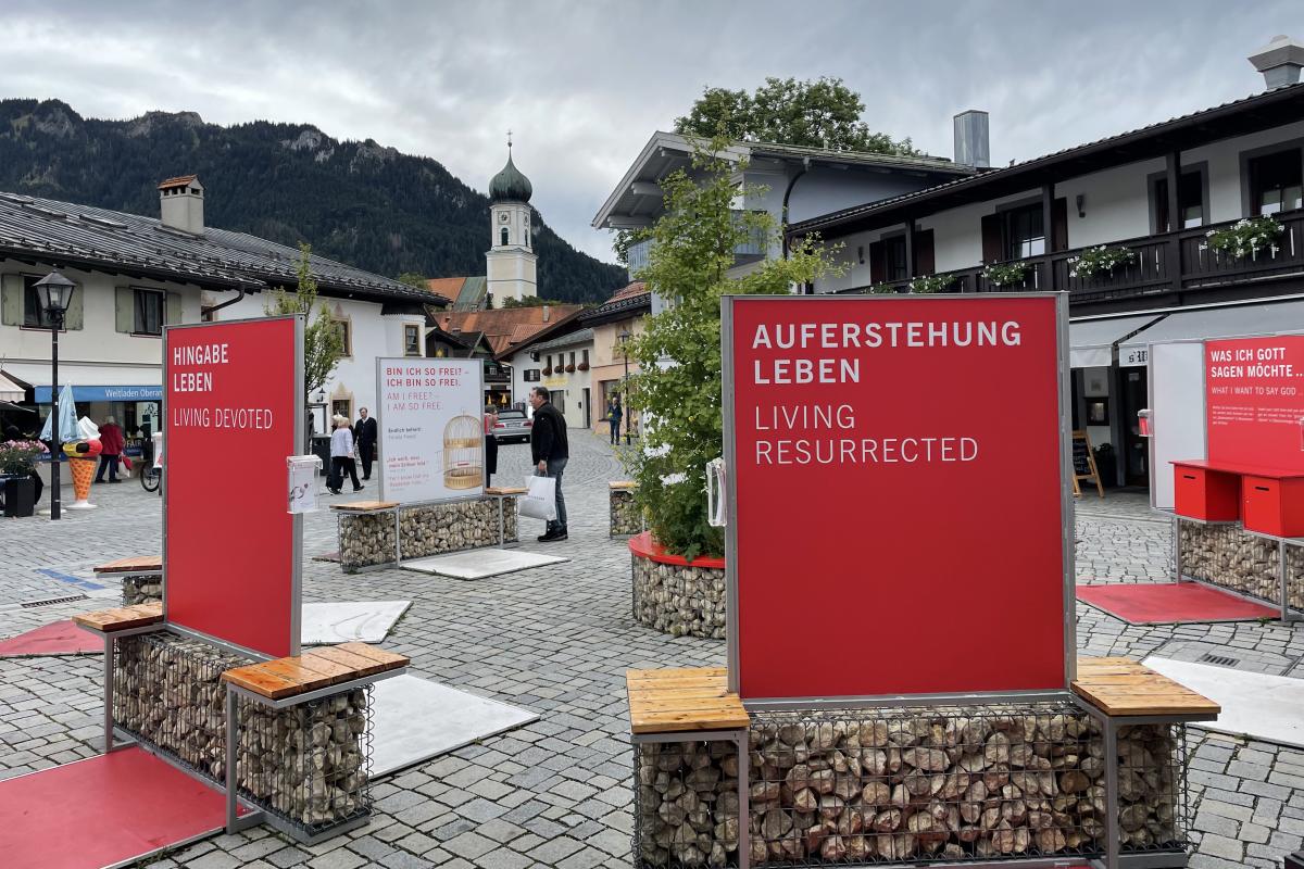 Red signs in a town square are part of an exhibit by the Catholic and Protestant churches in the village to promote religious reflection during the play. The spire of the Catholic church can be seen in the background.