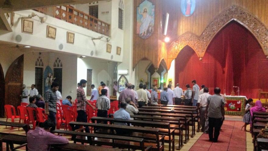 Male worshippers, seated on the left, line up to receive Prasadam after Mass at St. Mary Queen of Peace Basilica, Trivandrum.