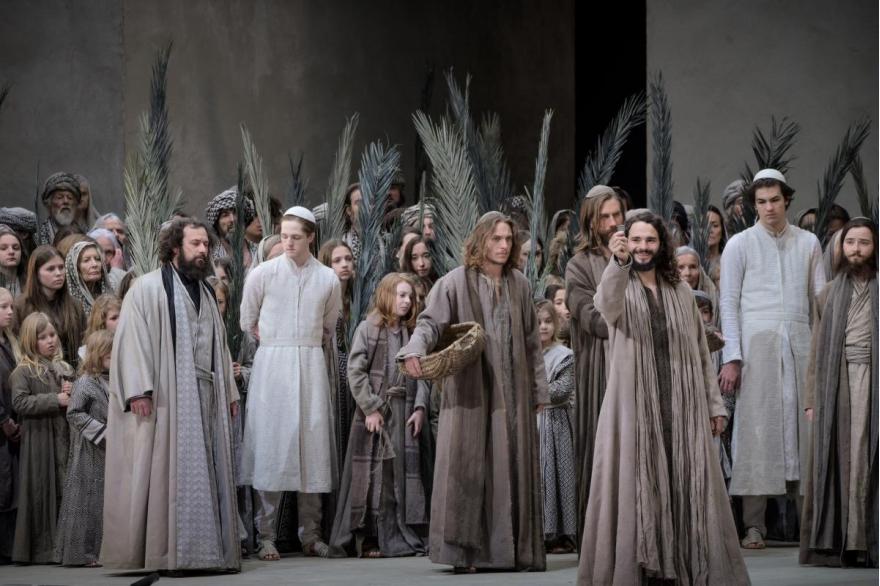 Jesus, front right, smiles and holds up a silver coin as people of Jerusalem surround him with palm fronds.