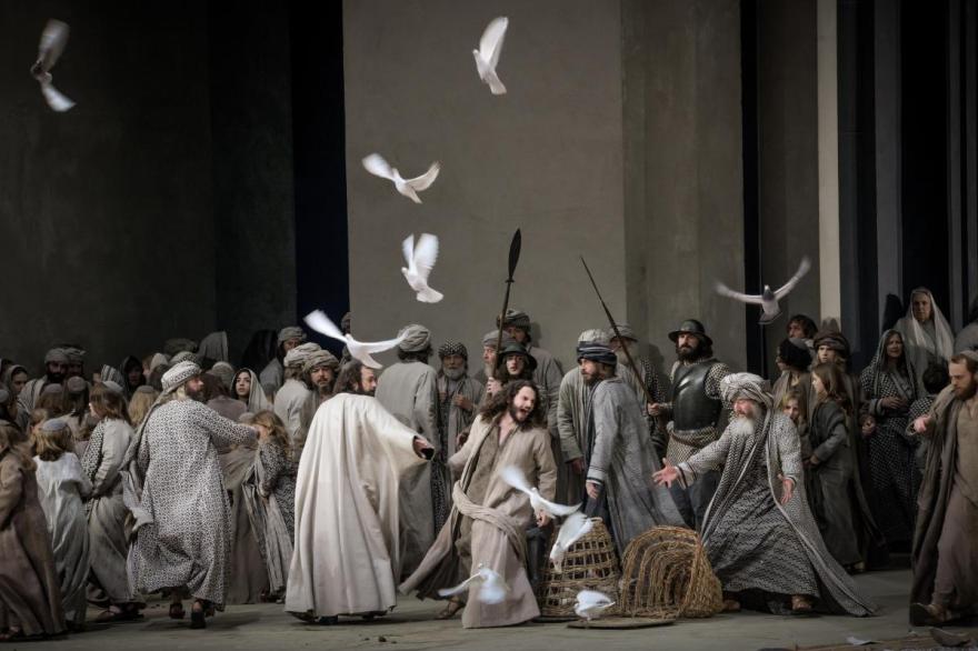 Doves are released as Jesus tips a basket in a marketplace filled with people.