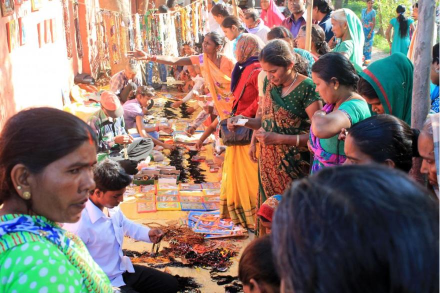 Vendors kneel on mats selling rosaries, candles and religious images to a crowd of shoppers.