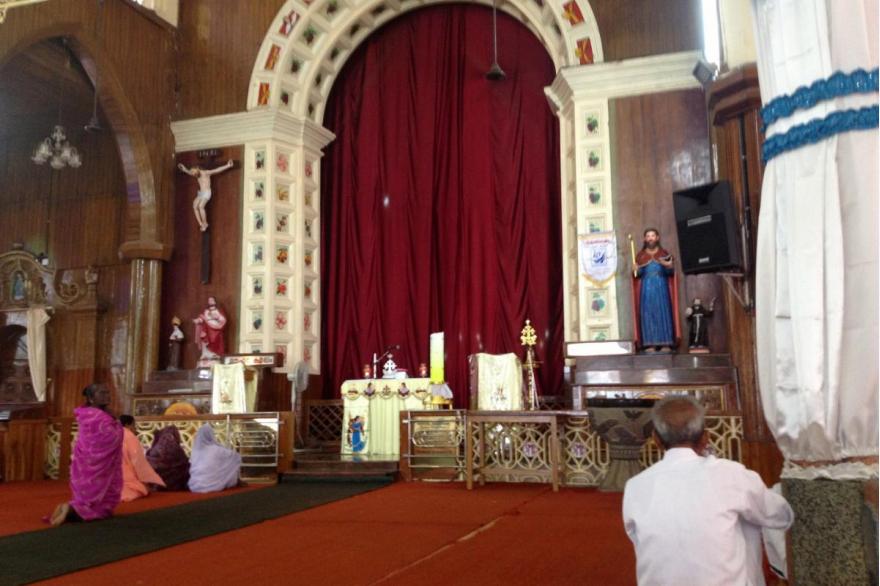 Worshipers arrive early to pray at St. Mary's Forane Church, a Syro-Malabar Church. The red drape covering the sanctuary is opened during liturgy.